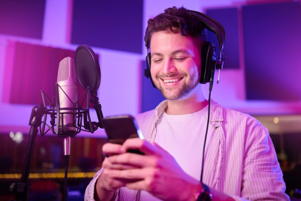 Man, Phone And Smile In Music Studio Chatting, Social Media Or Podcast Post At The Workplace. Happy Male Auto Tuner Smiling On Smartphone For Networking and social proof
